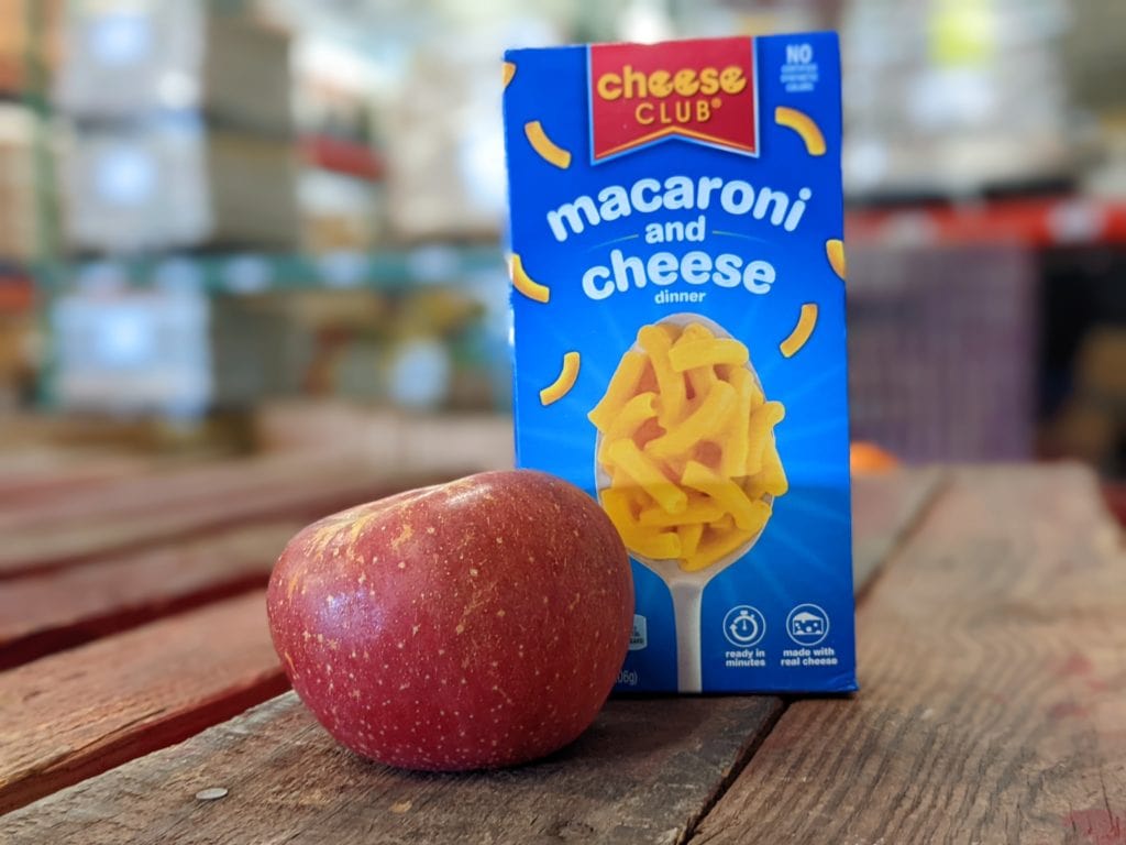 An apple and a box of mac and cheese on a wooden pallet