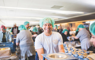 A man in a blue hairnet packs food for families overseas at a Feed My Starving Children MobilePack event.